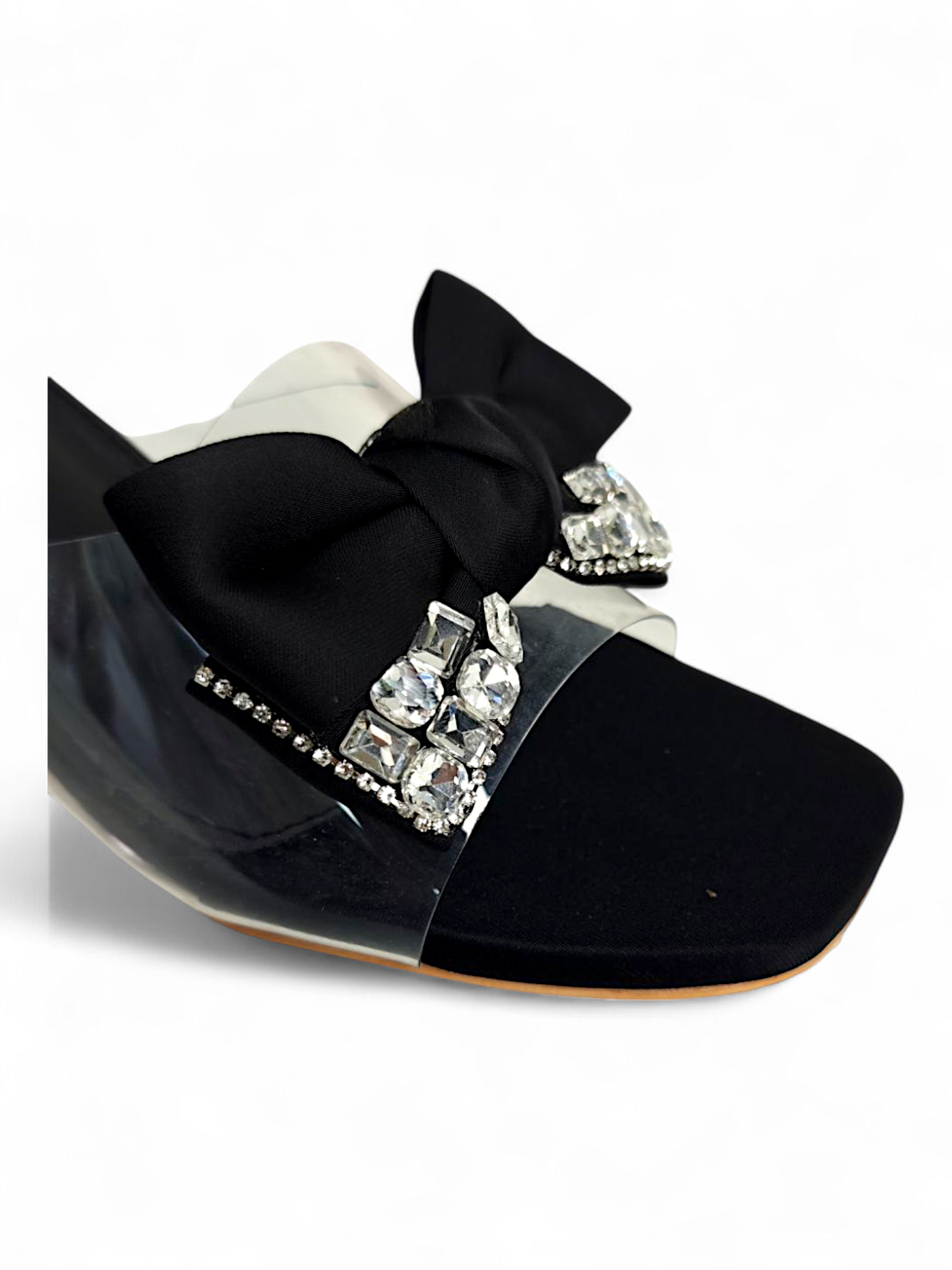 Close-up of decorative bow and rhinestone detailing on black clear strap sandals