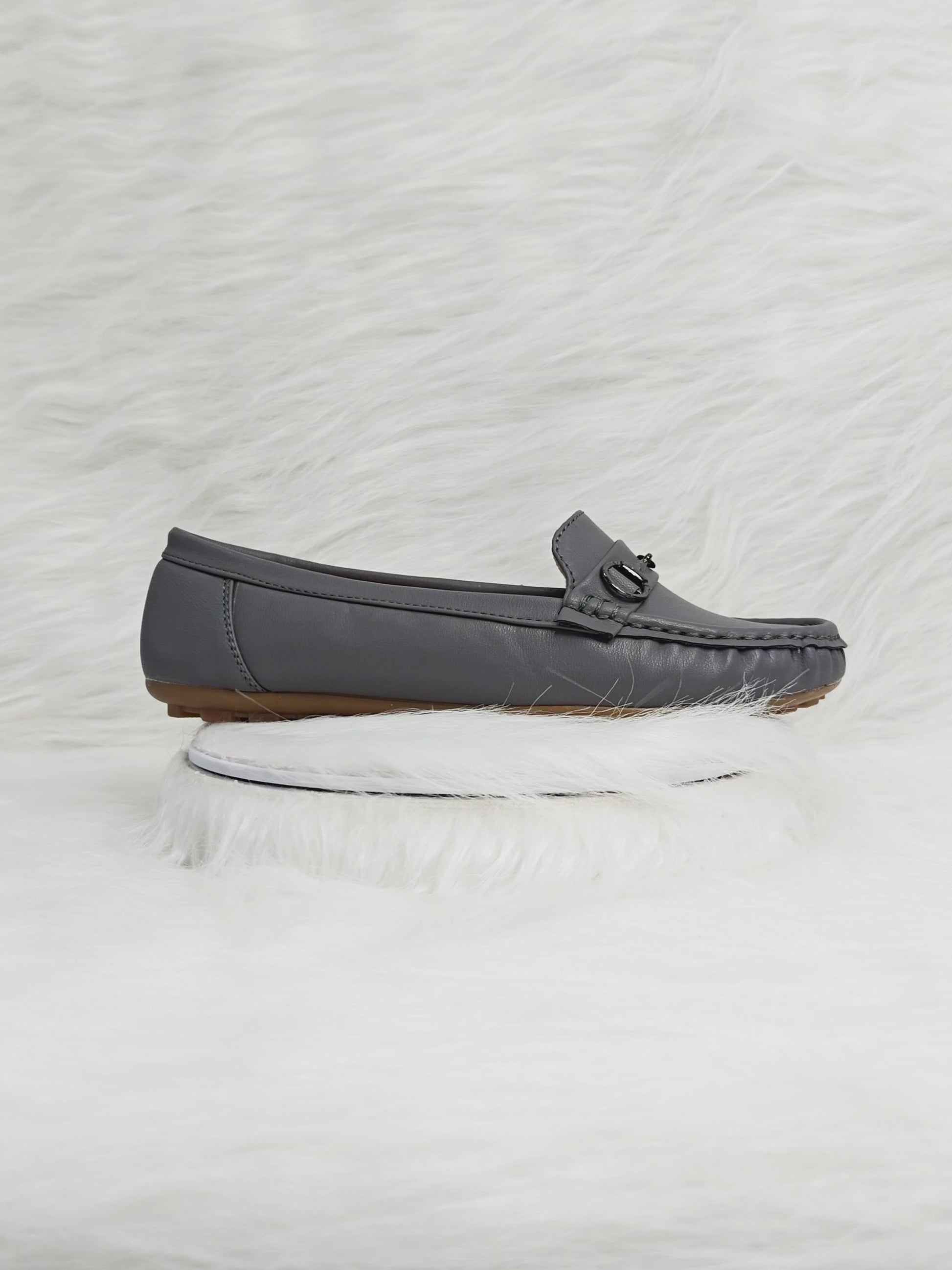 A close-up 360° video of grey women’s loafers with a metallic buckle detail and soft faux leather finish. The video highlights the cushioned insole, flexible sole, and elegant silhouette — ideal for office, casual, and daily wear.