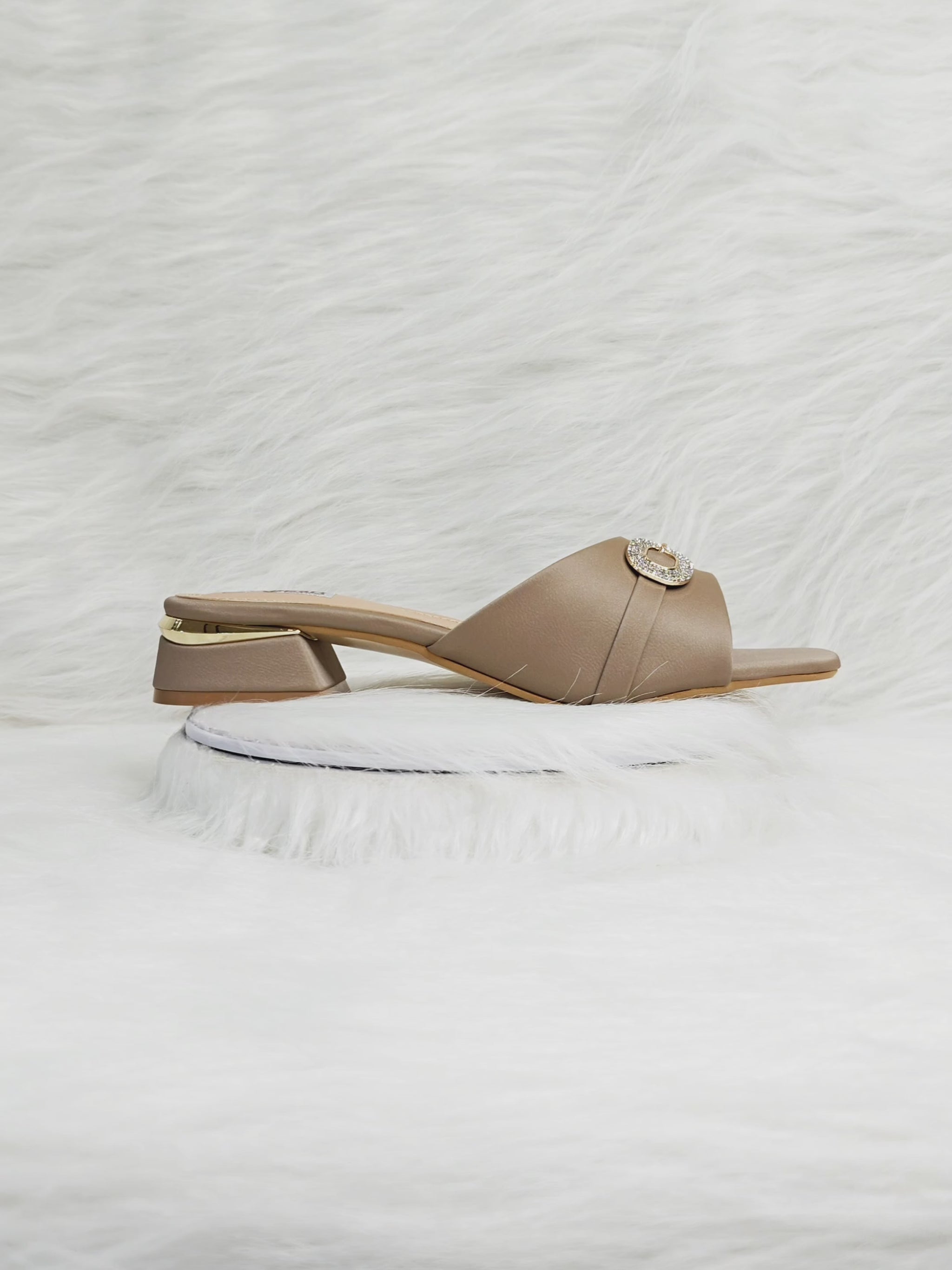 A woman walking comfortably in beige low-heel slippers featuring a crystal buckle, showing stability and style for daily wear.