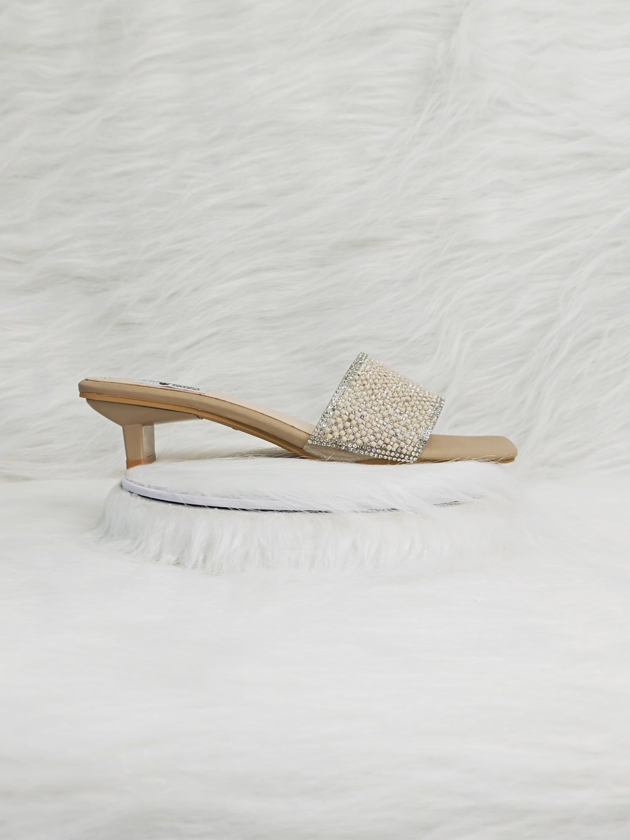 A close-up 360° video of beige crystal embellished heel sandals for women, highlighting the sparkling crystal strap, cushioned insole, and stylish block heel. Ideal for party, wedding, and festive wear.